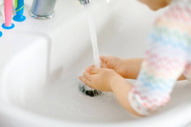 Küçük bir kızın banyoda ellerini sabunla ve suyla yıkaması. Çocuğun vücut parçalarını temizlemeyi öğrenmesini kapat. Virüs salgını sırasında yapılan hijyen rutini. Çocuk evde ya da çocuk odasında..