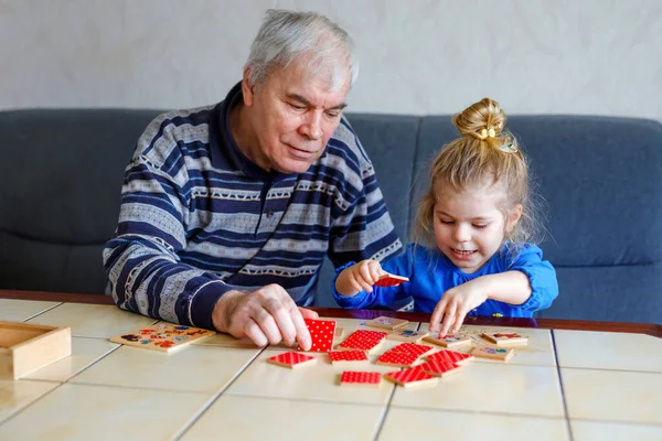 Krásná batole dívka a dědeček spolu hrají obrázky stolní karty doma. Roztomilé dítě a starší muž baví spolu. Šťastná rodina uvnitř — Stock fotografie