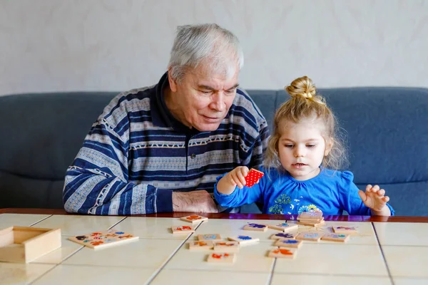 Krásná batole dívka a dědeček spolu hrají obrázky stolní karty doma. Roztomilé dítě a starší muž baví spolu. Šťastná rodina uvnitř — Stock fotografie