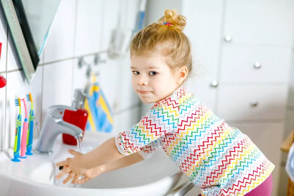 Linda niña pequeña lavándose las manos con agua y jabón en el baño. Adorable niño aprendiendo a limpiar partes del cuerpo. Acción rutinaria de higiene durante la enfermedad viral. niño en casa o guardería. — Foto de Stock