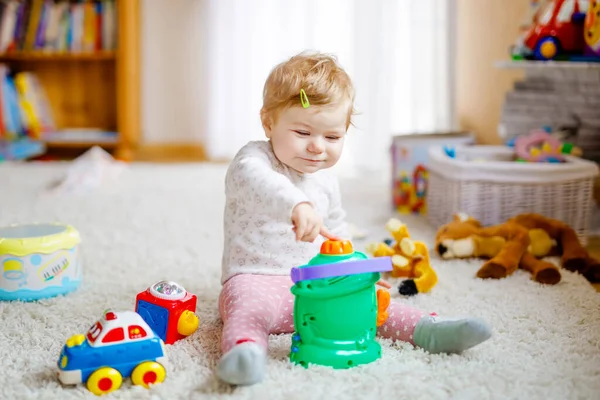 Šťastná radostná holčička hrající si s různými barevnými hračkami doma. Rozkošné zdravé batole dítě baví hrát sám. Aktivní volný čas v interiéru, školce nebo divadelní škole. — Stock fotografie