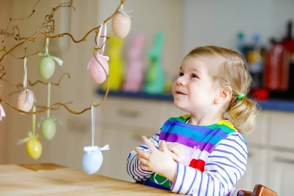 Aranyos kislány, aki faágat díszít színes pasztell műanyag tojással. Boldog kisbaba szórakozás húsvéti dekoráció. Imádnivaló egészséges mosolygós gyerek élvezi a családi nyaralás — Stock Fotó