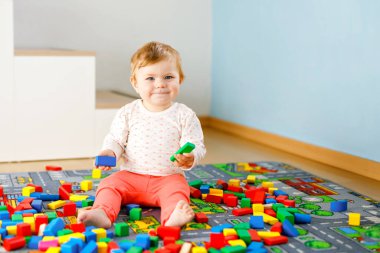 Eğitici oyuncaklarla oynayan sevimli bir kız bebek. Mutlu sağlıklı bir çocuk, evdeki renkli tahta bloklarla eğleniyor. Bebek öğrenme renkleri ve biçimleri