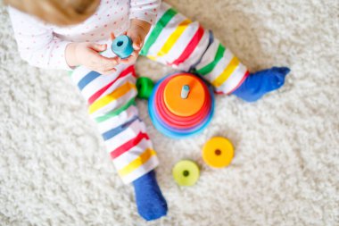 Evde ya da çocuk odasında eğitici oyuncaklarla oynayan sevimli, güzel bir kız bebek. Mutlu sağlıklı çocuk renkli ahşap çocuk oyuncak piramidiyle eğleniyor. Çocuk farklı yetenekler öğreniyor