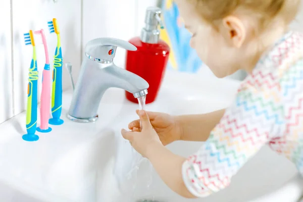 Primer plano de la niña pequeña lavándose las manos con agua y jabón en el baño. Primer plano del niño aprendiendo a limpiar partes del cuerpo. Acción rutinaria de higiene durante la enfermedad viral. niño en casa o guardería. — Foto de Stock