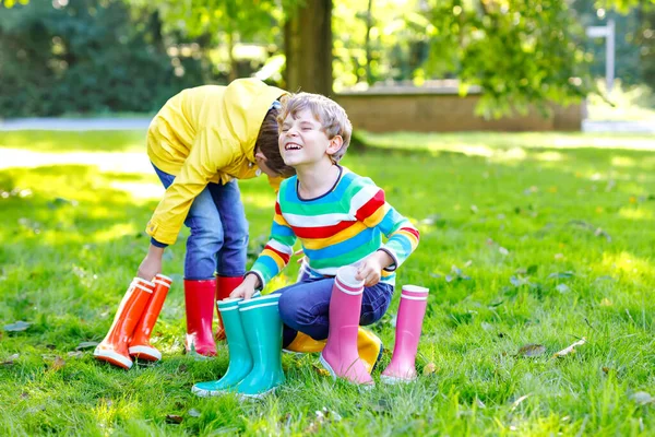 İki küçük çocuk, bir sürü renkli çizmeli şirin kardeşler. Farklı lastik botlar ve ceketler giymiş çocuklar. Yağmurlu bir sonbahar için ayakkabılar. Sağlıklı ikizler ve en iyi arkadaşlar dışarıda eğleniyorlar. — Stok fotoğraf