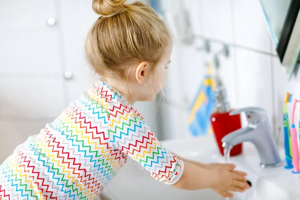 Linda niña pequeña lavándose las manos con agua y jabón en el baño. Adorable niño aprendiendo a limpiar partes del cuerpo. Acción rutinaria de higiene durante la enfermedad viral. niño en casa o guardería. — Foto de Stock