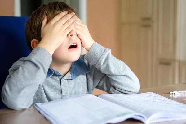 Rozrušený školák, který si během karantény dělá domácí úkoly na pandemii korony. Pláč a smutný chlapec frustrující pobyt doma. — Stock fotografie