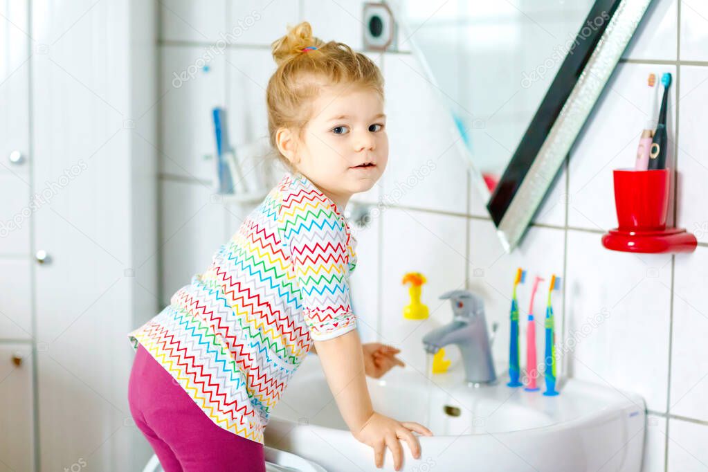 Cute little toddler girl washing hands with soap and water in bathroom. Adorable child learning cleaning body parts. Hygiene routine action during viral desease. kid at home or nursery.