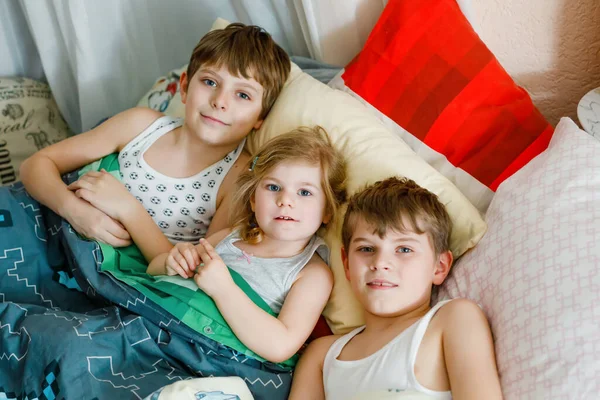 Τρία μικρά παιδιά σε καραντίνα ενάντια στον κορωνοϊό που παίζουν μαζί στο σπίτι. Δύο σχολιαρόπαιδα και ένα νήπιο διασκεδάζουν μέσα. Ενεργά παιδιά. Μείνετε στο σπίτι έννοια. — Φωτογραφία Αρχείου