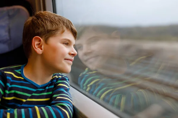 Schattige jongen die met de trein reist. Vrolijk lachend kind dat uit het raam kijkt terwijl de trein beweegt. Kind droomt en vraagt zich af. Familie vakanties en reis reis. — Stockfoto