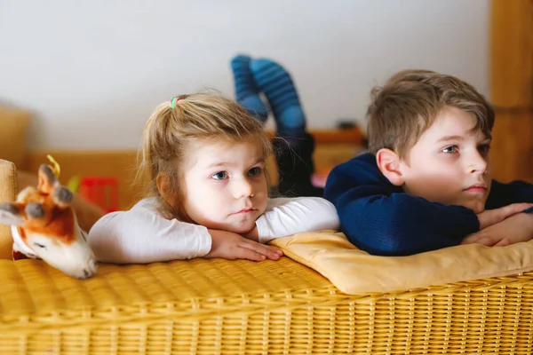 Χαριτωμένο κοριτσάκι και σχολιαρόπαιδο που βλέπει ταινία ή ταινία στην τηλεόραση. Ευτυχισμένα υγιή παιδιά, αδέλφια κατά τη διάρκεια της καραντίνας του κορωνάβιου να μένουν στο σπίτι. Αδελφός και αδελφή μαζί. — Φωτογραφία Αρχείου