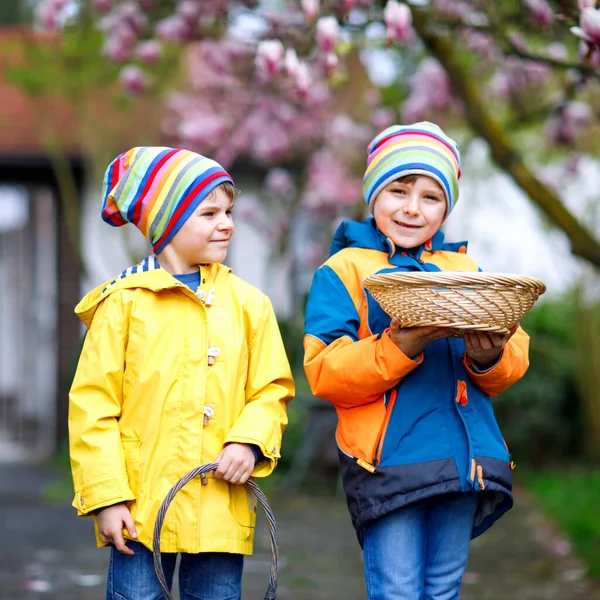 Duas crianças meninos e amigos fazendo tradicional caça ao ovo de Páscoa no jardim da primavera, ao ar livre. Irmãos se divertindo com a descoberta de ovos coloridos. No dia frio. Velha tradição cristã e católica . — Fotografia de Stock