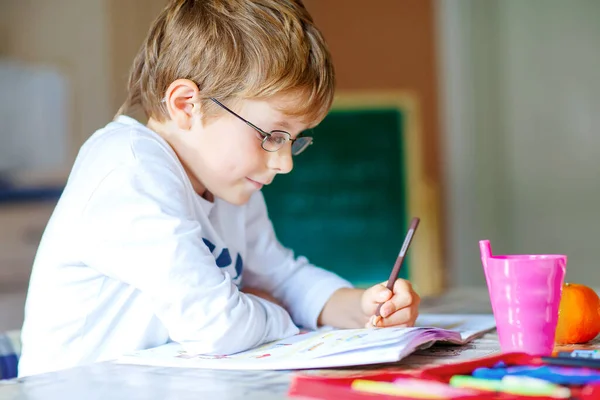 Hard werkende, vrolijke schooljongen die huiswerk maakt tijdens quarantainetijd door een corona pandemie. Gezond kind schrijven met pen, thuis blijven. Begrip "thuisonderwijs" — Stockfoto