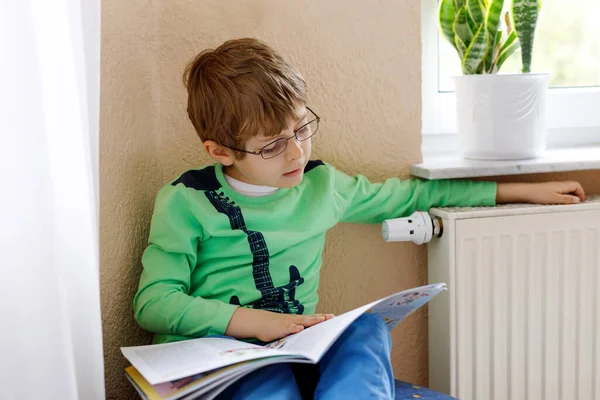 Hard-working happy school kid boy making homework during quarantine time from corona pandemic disease. Healthy child writing with pen, staying at home. Homeschooling concept