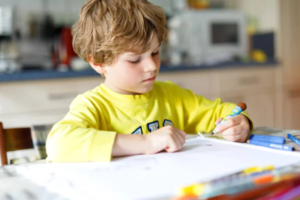 Hard werkende, vrolijke schooljongen die huiswerk maakt tijdens quarantainetijd door een corona pandemie. Gezond kind schrijven met pen, thuis blijven. Begrip "thuisonderwijs" — Stockfoto