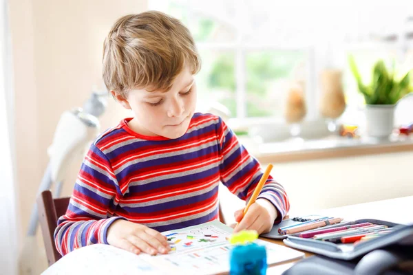 Hårt arbetande glad skolpojke gör läxor under karantänstid från koronapandemisk sjukdom. Friska barn skriva med penna, stanna hemma. Hemskolekoncept — Stockfoto