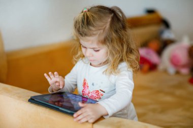 Evde tabletle oynayan tatlı küçük bir kız çocuğu. Sağlıklı bebek parmaklarıyla dokunuyor, çizgi film seyrediyor ve bilgisayardaki eğitici oyunlarla eğleniyor. Koronavirüse karşı karantina altında