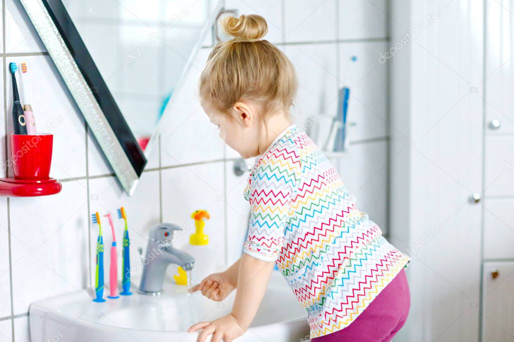 Cute little toddler girl washing hands with soap and water in bathroom. Adorable child learning cleaning body parts. Hygiene routine action during viral desease. kid at home or nursery.