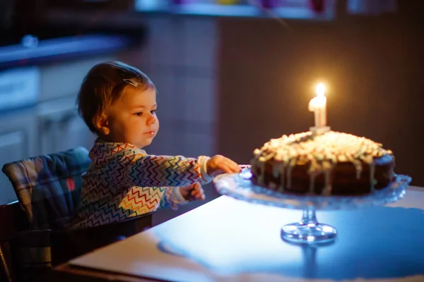 Ładny piękny dziewczynka świętuje pierwsze urodziny. Dziecko dmucha jedną świecę na domowej roboty pieczone ciasto, wewnątrz. Urodziny rodzinne przyjęcie dla uroczego dziecka malucha, piękna córka — Zdjęcie stockowe