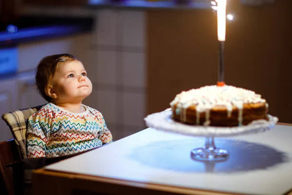Bella e carina bambina che festeggia il suo primo compleanno. Bambino che soffia una candela sulla torta al forno fatta in casa, al coperto. Festa di famiglia di compleanno per il bambino bello del bambino, bella figlia — Foto Stock