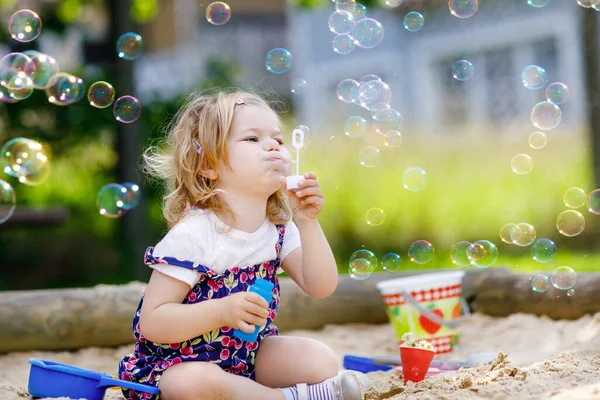 Gyönyörű szőke kislány, aki jól érzi magát szappanbuborék fúvóval. Aranyos baba gyermek játszik játszótéren napsütéses nyári napon. Boldog aktív vicces egészséges gyerek — Stock Fotó