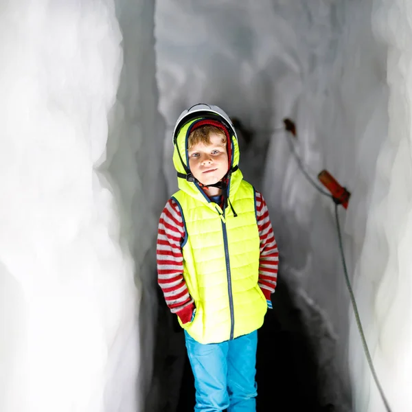 Liten pojke med säkerhetshjälmar inne i glaciären med istunnel. Skolbarn vandring och upptäcka berg i Tyrolen, Österrike, Hintertux. — Stockfoto