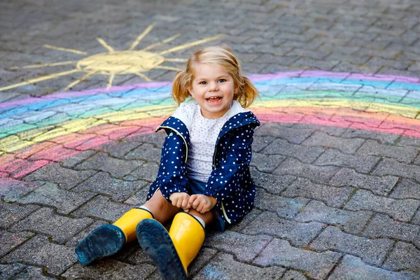 Felice bambina in stivali di gomma con arcobaleno dipinto con gessetti colorati a terra durante la quarantena pandemica coronavirus. Bambini che dipingono arcobaleni insieme alle parole Lascia che tutto vada bene — Foto Stock