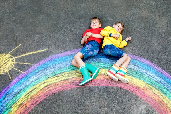 Twee schooljongens met regenboog beschilderd met kleurrijke krijtjes op de grond tijdens pandemische coronavirus quarantaine. Kinderen schilderen regenbogen samen met de woorden Laten we allemaal goed zijn. — Stockfoto