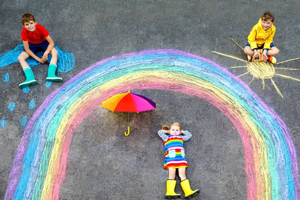 Tre bambini, due bambini della scuola ragazzi e bambina con arcobaleno dipinto con gessetti colorati durante la quarantena del coronavirus pandemico. Bambini che dipingono arcobaleni insieme alle parole Lascia che tutto vada bene . — Foto Stock