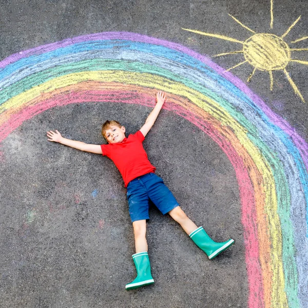 Gelukkige jongen met regenboog geschilderd met kleurrijke krijtjes op de grond tijdens pandemische coronavirus quarantaine. Kinderen schilderen regenbogen samen met de woorden Laten we allemaal goed zijn. — Stockfoto