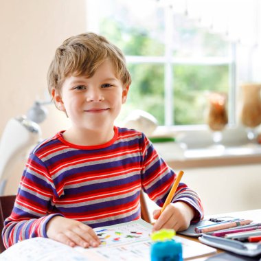 Hard-working happy school kid boy making homework during quarantine time from corona pandemic disease. Healthy child writing with pen, staying at home. Homeschooling concept clipart
