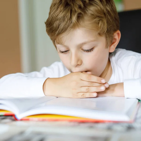 Hard-working happy school kid boy making homework during quarantine time from corona pandemic disease. Healthy child writing with pen, staying at home. Homeschooling concept