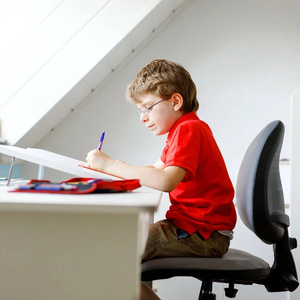 Hårt arbetande glad skolpojke gör läxor under karantänstid från koronapandemisk sjukdom. Friska barn skriva med penna, stanna hemma. Hemskolekoncept — Stockfoto