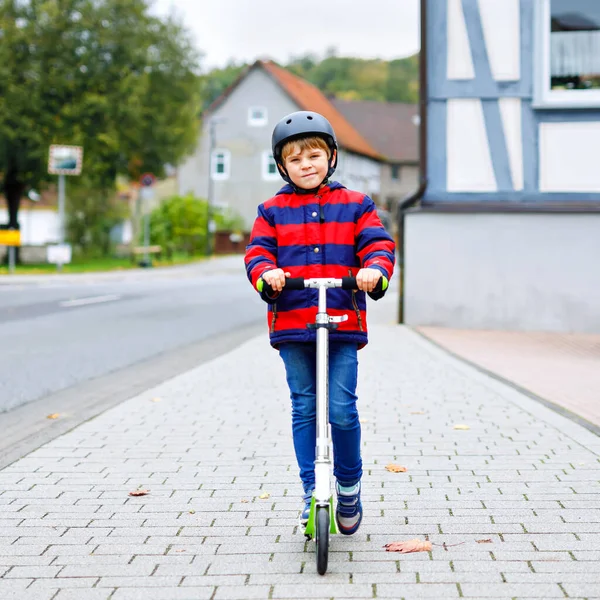 Carino ragazzino della scuola con casco cavalcando su scooter nella natura parco. attività per bambini all'aperto in inverno, primavera o autunno. divertente bambino felice in abiti colorati moda . — Foto Stock