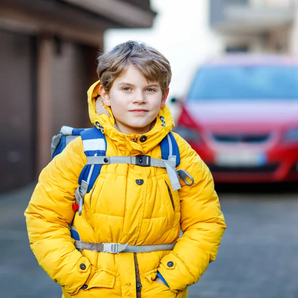 Petit écolier du primaire marchant jusqu'à l'école. Portrait d'enfant heureux dans la rue avec la circulation. Étudiant avec veste jaune et sac à dos en vêtements d'hiver colorés. — Photo