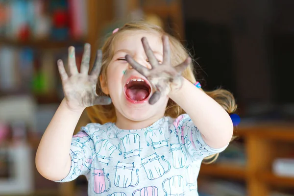 Linda niña adorable aprendiendo pintura con acuarelas. Pequeño dibujo infantil en casa, utilizando pinceles de colores. Niño feliz y saludable con la cara y las manos sucias en casa o en el vivero —  Fotos de Stock