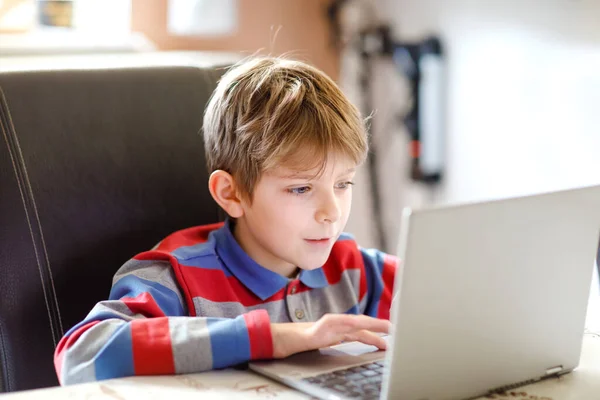 En liten skolunge som gör läxor på datorn. Barn lär sig på datorn. Hårt arbetande pojke gör motion under karantänstid från koronapandemisk sjukdom. Hemskolekoncept. — Stockfoto