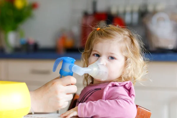 Menina pequena fazendo inalação com nebulizador em casa. Pai ou mãe ajudando e segurando o dispositivo. Criança com gripe, tosse e bronquite. asma inalador inalação vapor conceito doente — Fotografia de Stock