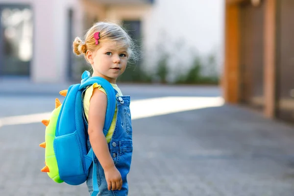 彼女の最初の日にかわいいかわいい幼児の女の子は学校に行く。保育園や幼稚園まで歩く健康な美しい赤ちゃん。街の通りのバックパックを持つ幸せな子供、屋外. — ストック写真