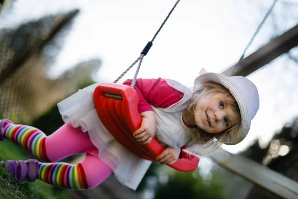 Söt förtjusande liten flicka svänger i inhemsk trädgård med mjuk plysch leksak. Glad frisk baby barn i hatt och klänning spelar utomhus på solig varm dag. — Stockfoto