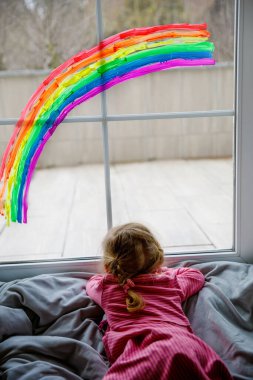 Salgın koronavirüs karantinası sırasında gökkuşağı rengine boyanmış sevimli küçük kız. Dünyanın dört bir yanında gökkuşağı çizen bir çocuk..