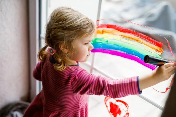 Mała dziewczynka Adoralbe z tęczą pomalowana kolorowym kolorem okna podczas pandemii kwarantanny koronawirusowej. Dziecko maluje tęcze na całym świecie słowami Niech wszystko będzie dobrze. — Zdjęcie stockowe