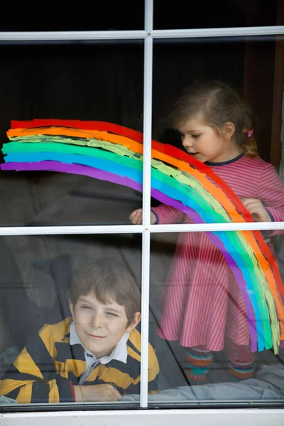 Zwei Kinder, Schuljunge und Kleinkind mit Regenbogen bemalt mit bunten Fensterfarben während der Coronavirus-Quarantäne-Pandemie. Kinder malen Regenbogen mit den Worten Lets all be well — Stockfoto