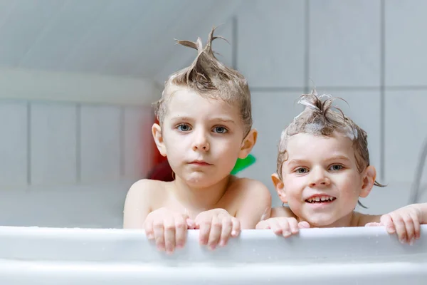 Happy siblings: Two little healthy twins children playing together with water by taking bath in bathtub at home. Kid boys having fun together. children washing heads and hairs with shampoo. — Stock Photo, Image