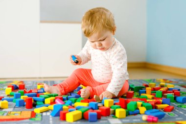 Eğitici oyuncaklarla oynayan sevimli bir kız bebek. Mutlu sağlıklı bir çocuk, evdeki renkli tahta bloklarla eğleniyor. Bebek öğrenme renkleri ve biçimleri