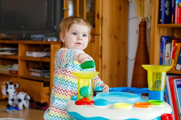 Happy joyful baby girl playing with different colorful toys at home. Adorable healthy toddler child having fun with playing alone. Active leisure indoors, nursery or playschool. — Stock Photo, Image