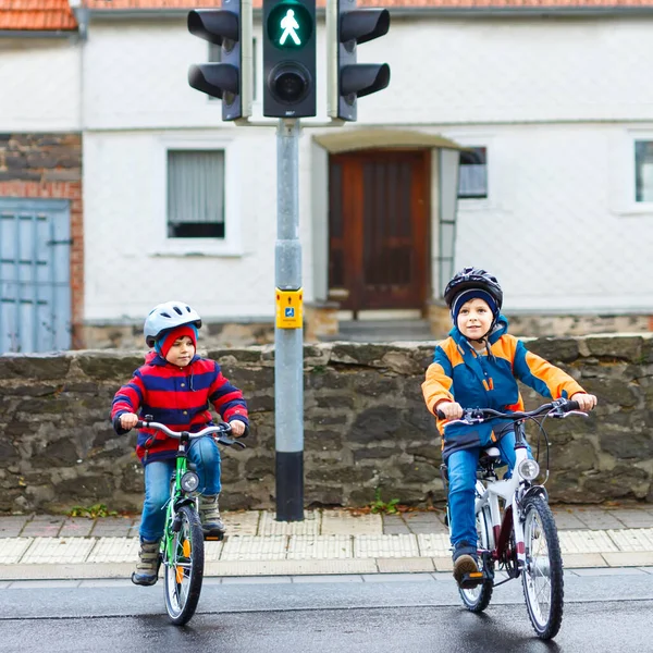 Dos chicos activos en bicicleta de casco en bicicletas en la ciudad. Niños felices con ropa colorida y esperando el semáforo verde. Seguridad y protección para niños en edad preescolar — Foto de Stock