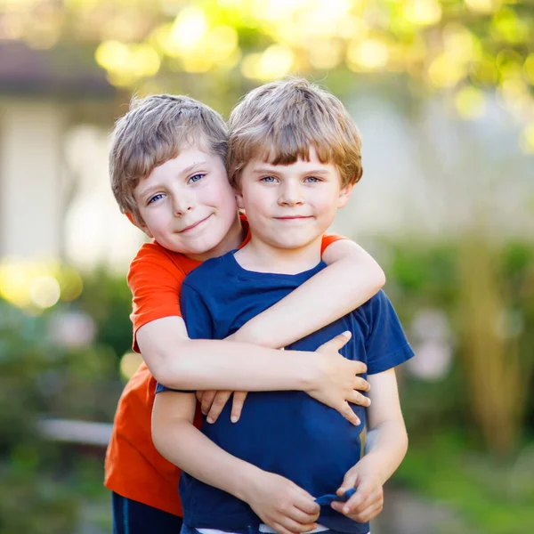 Två små aktiva skolpojkar, tvillingar och syskon som kramas på sommardagen. Söta bröder, förskolebarn och bästa vänner porträtt. Familj, kärlek, bindning koncept — Stockfoto