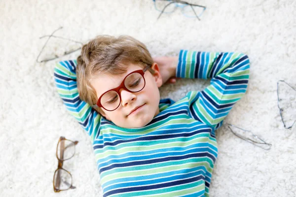 Close-up portrait of little blond kid boy with different eyeglasses on white background. Happy smiling child in casual clothes. Childhood, vision, eyewear, optician store. Boy choosing new glasses. — Stock Photo, Image